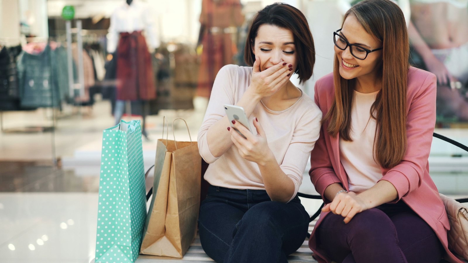 Two friends laughing at a phone while out shopping